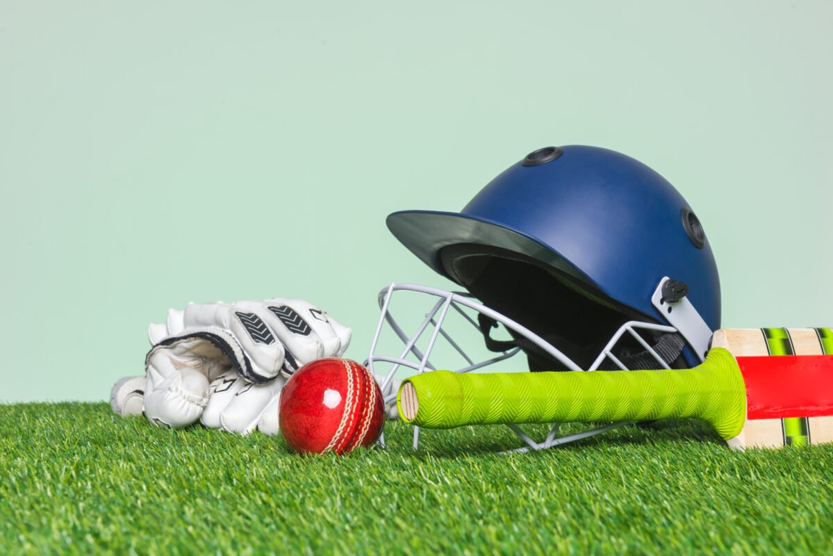 Cricket equipment with bat, ball, helmet and gloves on grass
